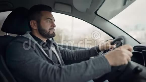 大胡子帅哥白天在城里开车车内侧视小伙子手拉方向盘视频的预览图
