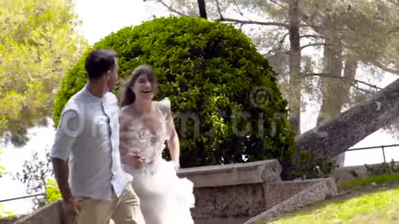 新婚夫妇夏天在公园里跑步行动美丽的情侣浪漫地在公园里牵手逃跑妻子视频的预览图