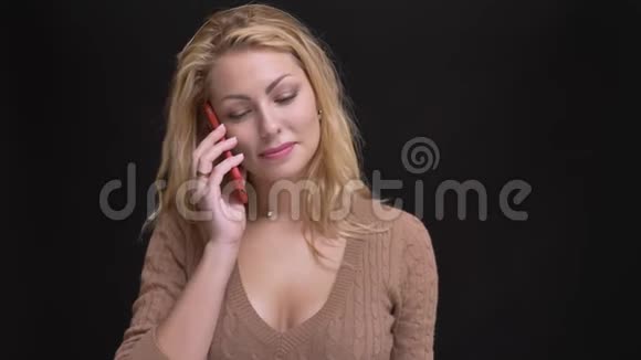 华丽的白种人长发女人在黑色背景的智能手机上微笑交谈的肖像视频的预览图
