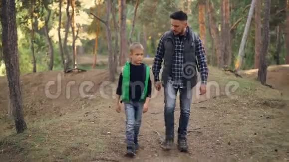 英俊的年轻人和他可爱的小儿子在森林里散步谈论新鲜的空气自然和自然视频的预览图