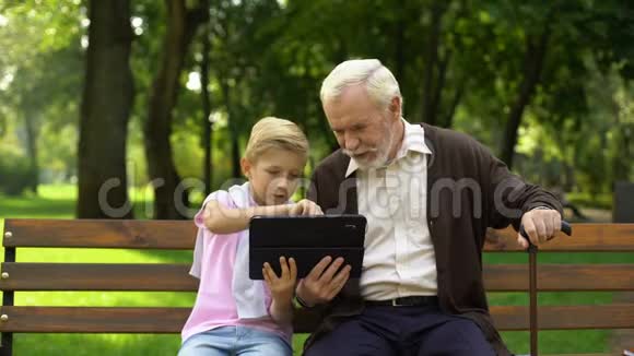 男孩向快乐的祖父展示平板电脑日常生活中的计算机技术视频的预览图
