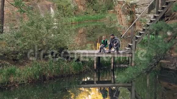 爱的父亲正在教他的儿子在秋日钓鱼人们坐在木墩上用棍子说话视频的预览图