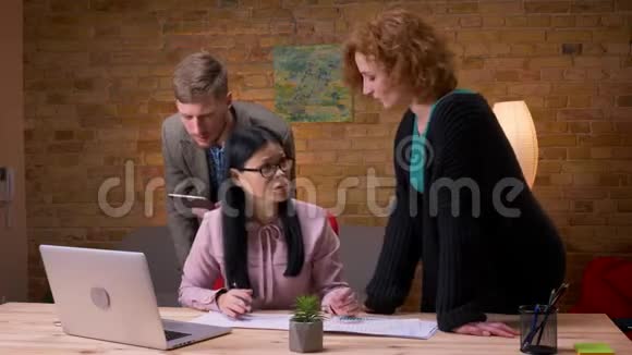 三名员工在办公室内使用笔记本电脑平板电脑和图表讨论数据的特写镜头视频的预览图