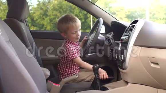 快乐的小男孩坐在汽车的车轮后面玩慢动作视频的预览图