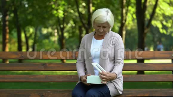 老太太坐在长凳上看着吊坠想起她的丈夫失落视频的预览图
