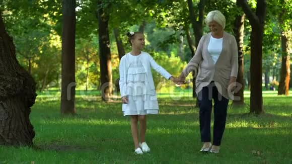 奶奶和孙女牵着手一起在公园里散步交流视频的预览图