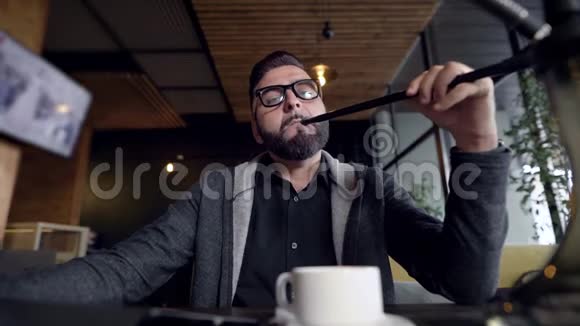 英俊的年轻人白天在一家餐馆抽烟在镜头前吐出烟站在桌子上视频的预览图