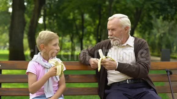 孙子和爷爷在公园吃香蕉有机水果健康的生活方式视频的预览图