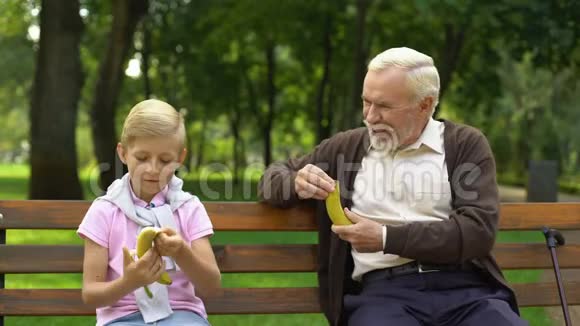 爷爷和男孩在公园里吃香蕉在户外吃零食健康的食物视频的预览图