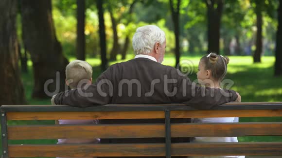 祖父和小孙子们讨论周末计划坐在长凳上视频的预览图