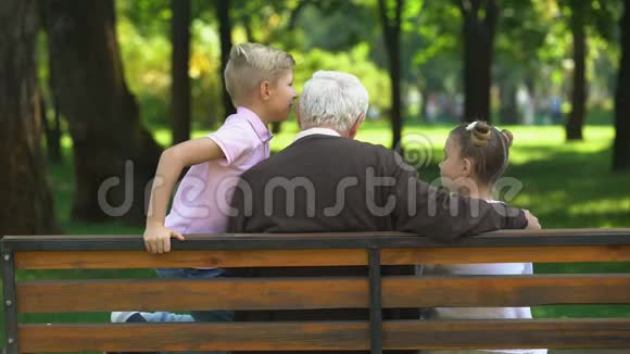 孩子们和祖父分享秘密在公园里的长椅上休息后景视频的预览图