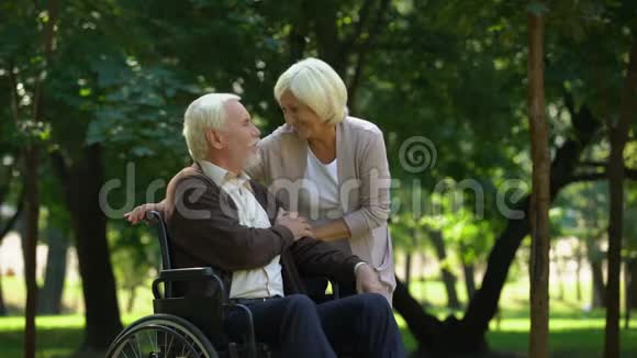 成熟的夫妇在公园里休息看着孙子坐在轮椅上的男人视频的预览图