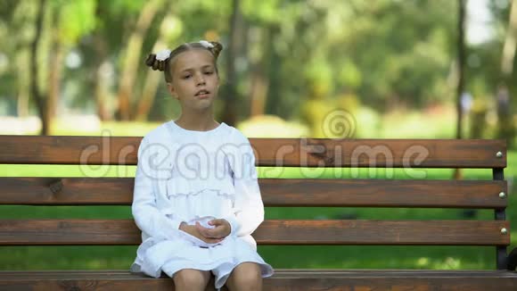 可爱的女学生独自坐在公园的长凳上环顾四周缺乏朋友视频的预览图