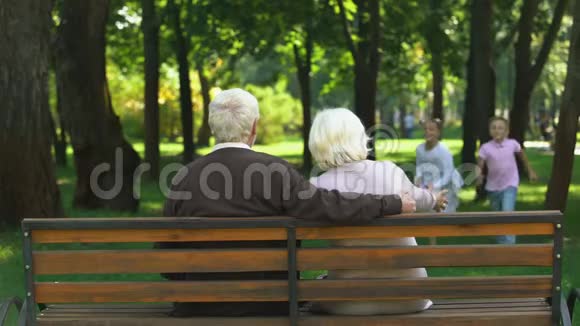 可爱的兄弟姐妹跑到祖父母坐在公共公园的长凳上家人视频的预览图