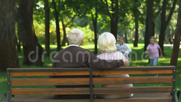 孙辈们跑到爷爷奶奶身边拥抱他们在公园的长椅上休息视频的预览图