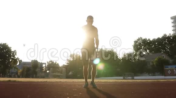 一个穿着黑色运动服的运动男子的全身在户外体育场训练前热身太阳视频的预览图