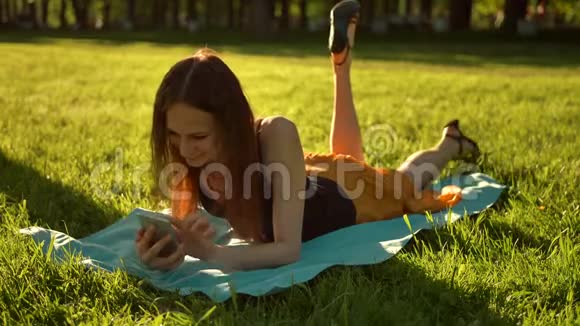一个英俊的女人躺在草地上打电话留言视频的预览图