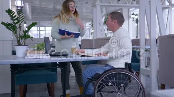 残疾快乐生病的学生轮椅上的成熟男子和使用智能计算机技术的女教育家的培训视频的预览图