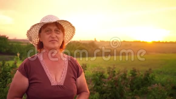 一位穿着棕色T恤和白色帽子的老妇人在夕阳下的肖像这位女士看着相机和视频的预览图