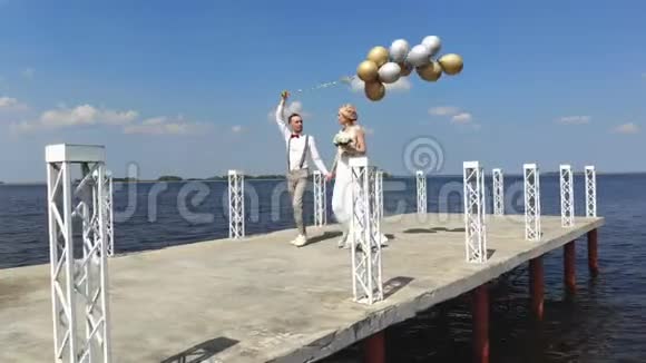年轻漂亮的新婚夫妇正走在美丽的码头上新郎手里拿着气球看着每一个人视频的预览图