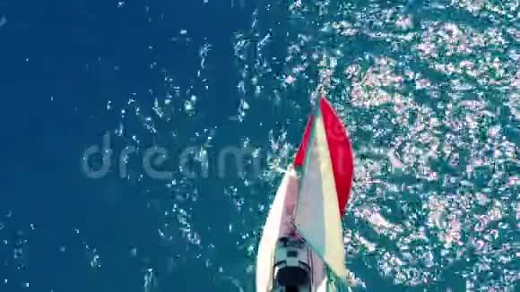 空中观景一艘美丽的帆船带着红色的帆正在阳光明媚的日子里在翡翠海上航行视频的预览图
