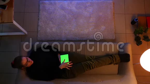 在舒适的室内沙发上躺着时一位漂亮的女性使用带有绿色屏幕的平板电脑进行特写拍摄视频的预览图