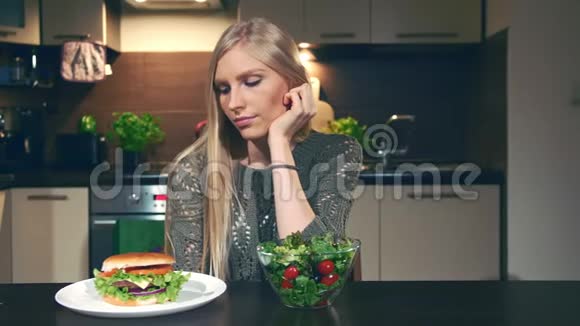 年轻女子在汉堡包和沙拉之间做出选择美丽的年轻女士在看美味的汉堡和健康的蔬菜视频的预览图