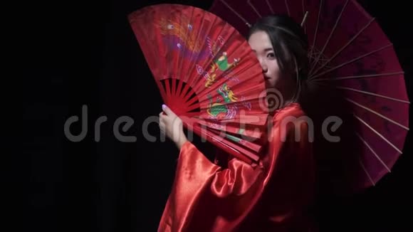 漂亮的东方女人带着红色的扇子和一把伞凝视着外面视频的预览图