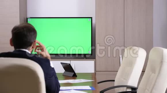 商人的后脑勺对着绿色屏幕电视说话视频的预览图