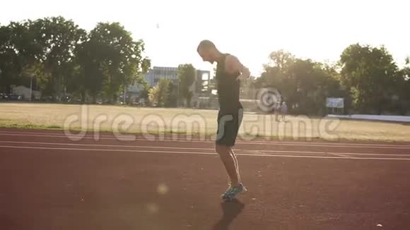 年轻运动员男性在体育场跑道上伸展双手准备跑步或训练的手持镜头视频的预览图