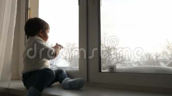 冬天男孩坐在一扇大窗户前挥手视频的预览图