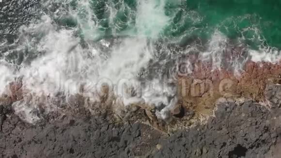 空中射击垂直计划拉下蓝色和绿松石色的海洋和海水起泡以及火山海岸线视频的预览图