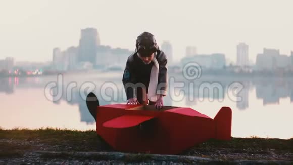 小快乐飞行员男孩进入有趣的红色纸板飞机服装在惊人的和平城市湖全景慢动作视频的预览图