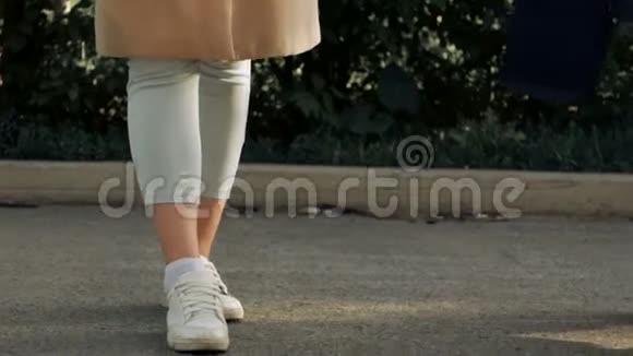 一个年轻的女孩带着婴儿车穿过公园在电话里交谈腿特写视频的预览图