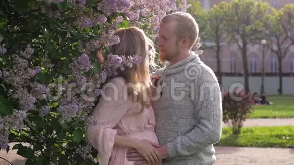 穿着粉红色裙子的孕妇和她丈夫一起散步已婚夫妇在开花的背景下怀孕视频的预览图