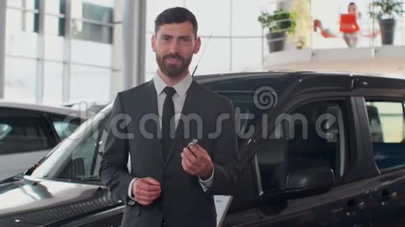 专业的汽车推销员微笑着幸福地拿着车钥匙站在经销商的新车前面视频的预览图