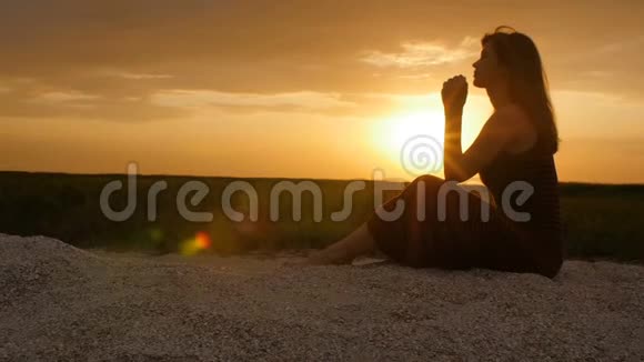 日落时分一位年轻女子在沙滩上的剪影女孩在地平线上向上帝祈祷度假的概念宗教Bea视频的预览图