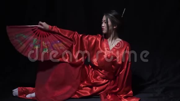 令人惊叹的年轻女子穿着红色日本国服带着扇子坐在地板上视频的预览图