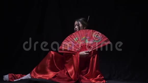 亚洲女人坐在地板上躲在扇子后面微笑视频的预览图