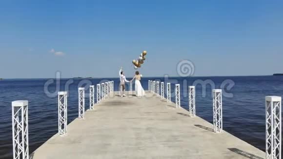 年轻漂亮的新婚夫妇正走在美丽的码头上新郎手里拿着气球看着每一个人视频的预览图