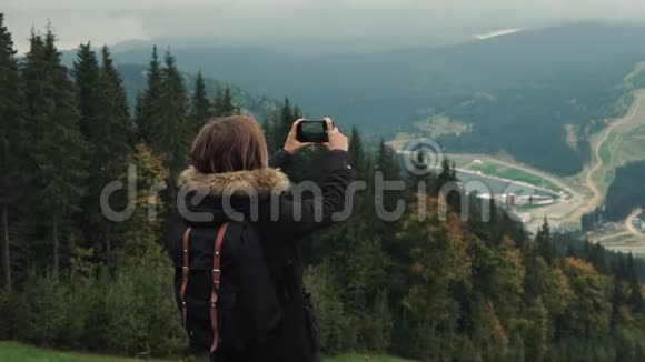 年轻女孩徒步旅行者正在手机相机上拍摄美丽的雾山景观视频视频的预览图