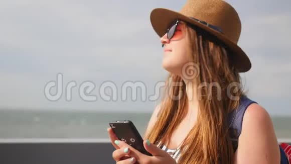 夏天戴帽子的年轻女孩在长廊散步留着电话计划在智能手机上拍照享受快乐视频的预览图