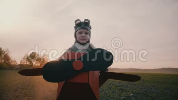 快乐的小男孩穿着有趣的纸板飞机服装沿着夕阳跑着秋天的田野玩着航空飞行员的慢动作视频的预览图