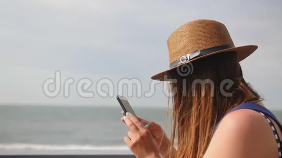 夏天戴帽子的年轻女孩在长廊散步留着电话计划在智能手机上拍照享受快乐视频的预览图