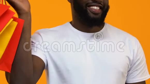 微笑的非洲男人带着购物袋在黄色背景上竖起大拇指视频的预览图