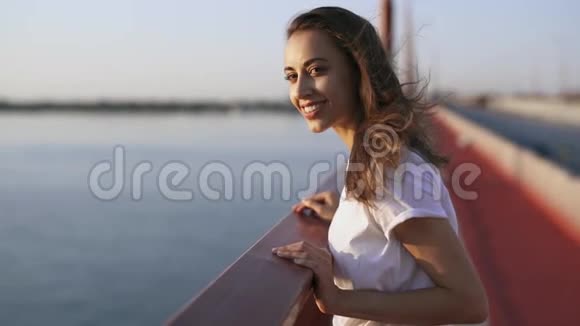 年轻快乐的女人看着傍晚的海上日落美丽的女孩站在桥上欣赏日落美景视频的预览图