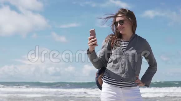 一个女人在大海的背景下在手机上自拍照片视频的预览图