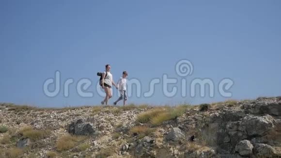 母亲和儿子一起在山上旅行他们到悬崖边上的草地上覆盖着贫瘠的山景视频的预览图