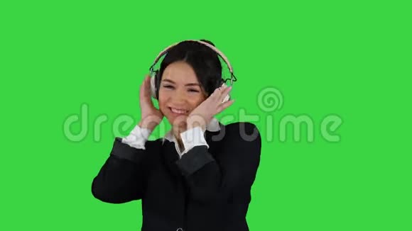 年轻的商务女性听着耳机里的音乐在绿色屏幕上跳舞Chroma键视频的预览图