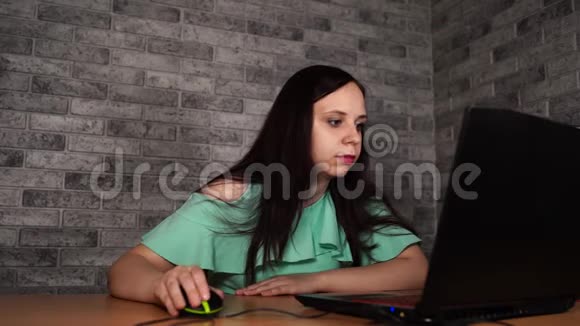 年轻女子坐在桌子旁用笔记本电脑深色头发的浓眉在工作时看着笔记本电脑的展示视频的预览图